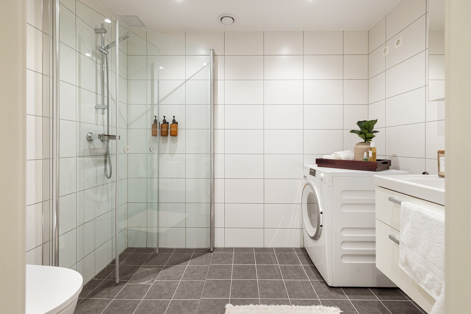 Badet fremstår som delikat og moderne med flislagte overflater, varmekabler i gulv og downlights i tak. Galleribilde
