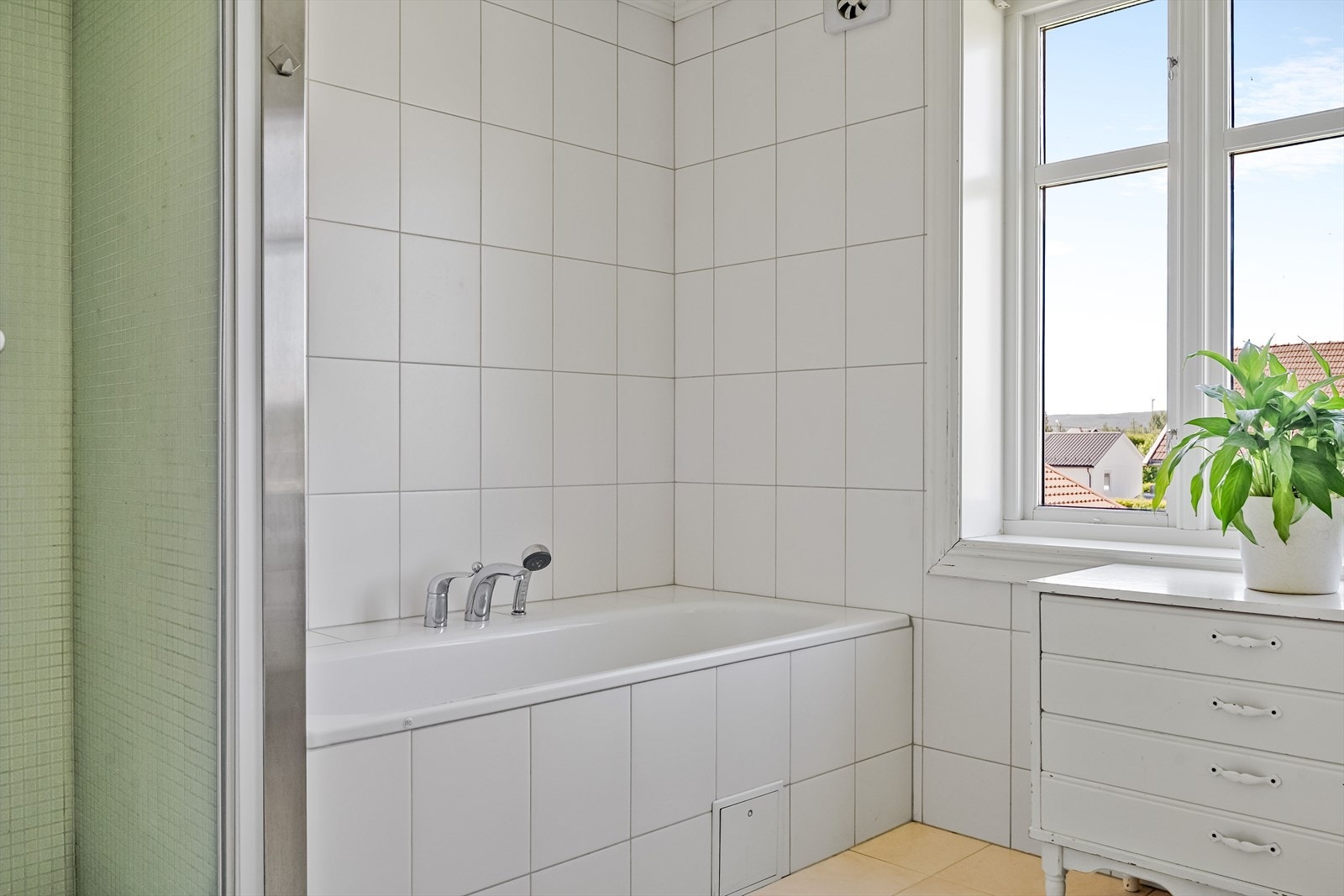 Innfliset badekar og dusjnisje med flislagt vegg og glassdør. Galleribilde