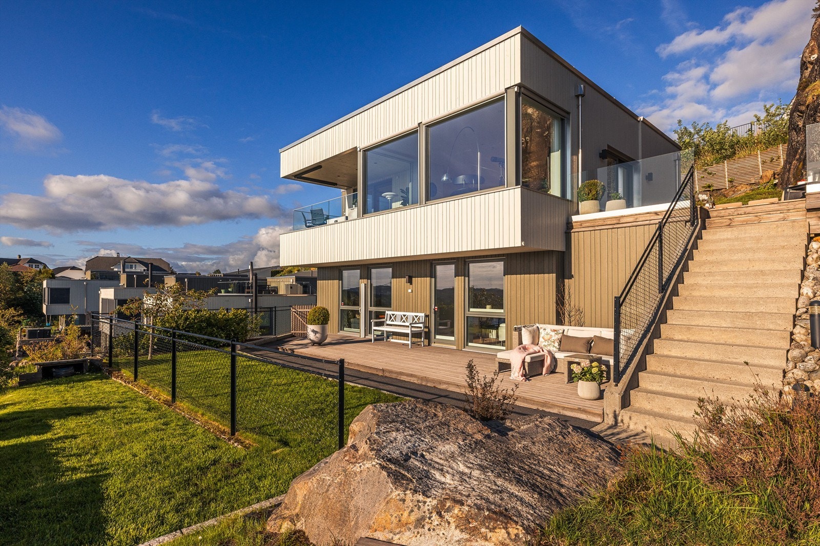 Eneboligen har en moderne arkitektur med store vinduer og rette linjer. Kledd med trekledning, rekkverk i glass og støpt trapp med belysning. Galleribilde