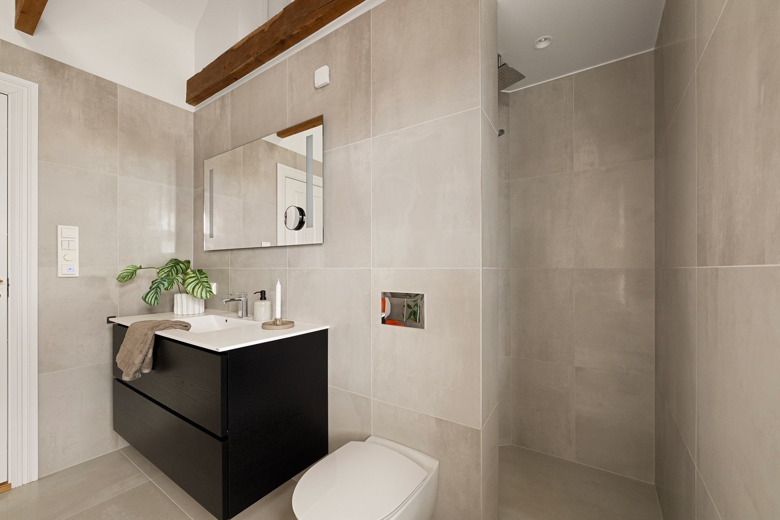 Badet har fliser på gulv og vegger, vegghengt toalett og en romslig dusjnisje. Galleribilde