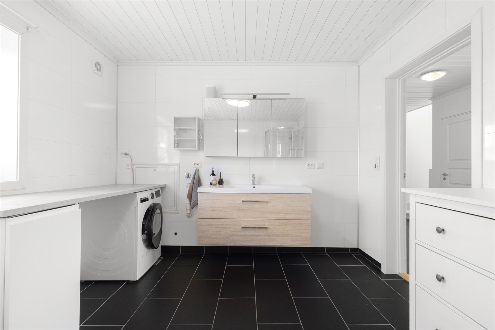 Innredning med laminat benkeplate og veggmontert servantinnredning med skuffer og hel servantplate, samt tilhørende speilskap med overlys. Galleribilde