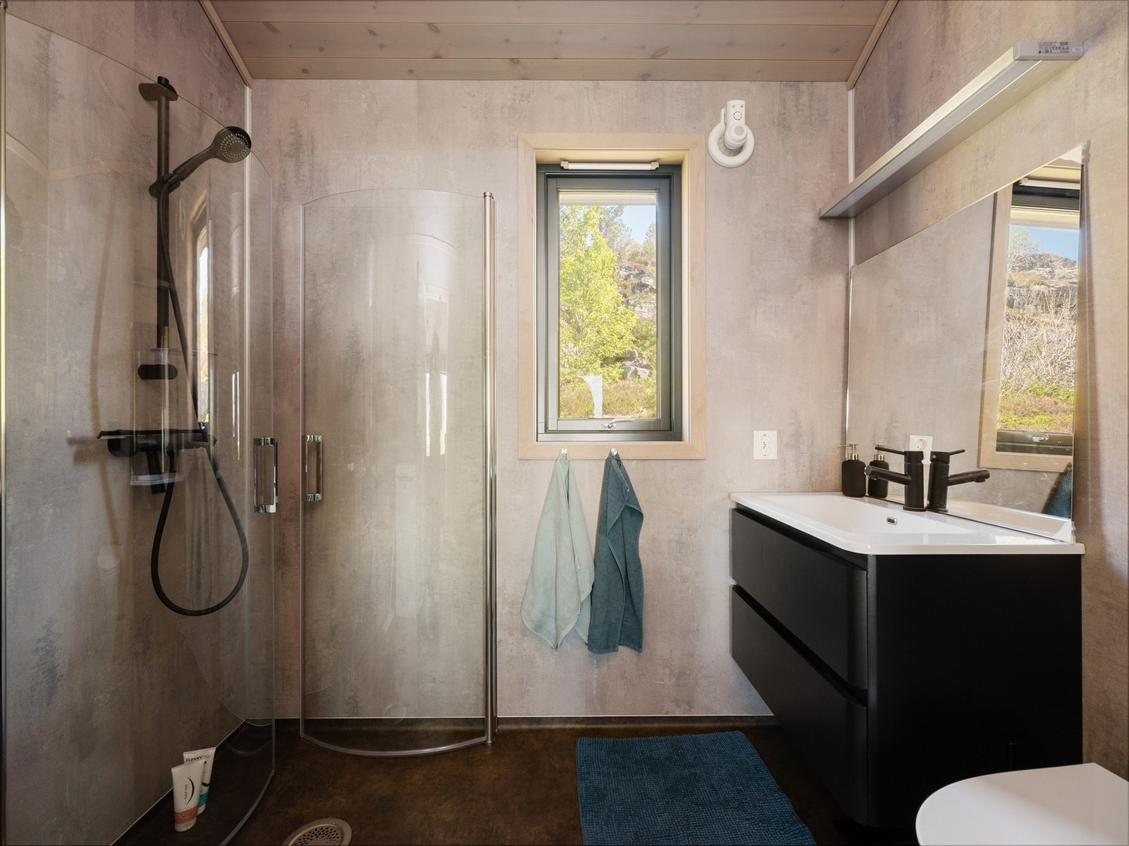 Badet har en moderne og praktisk utførelse med dusjløsning, servantinnredning, veggmontert toalett og opplegg for vaskemaskin. Galleribilde