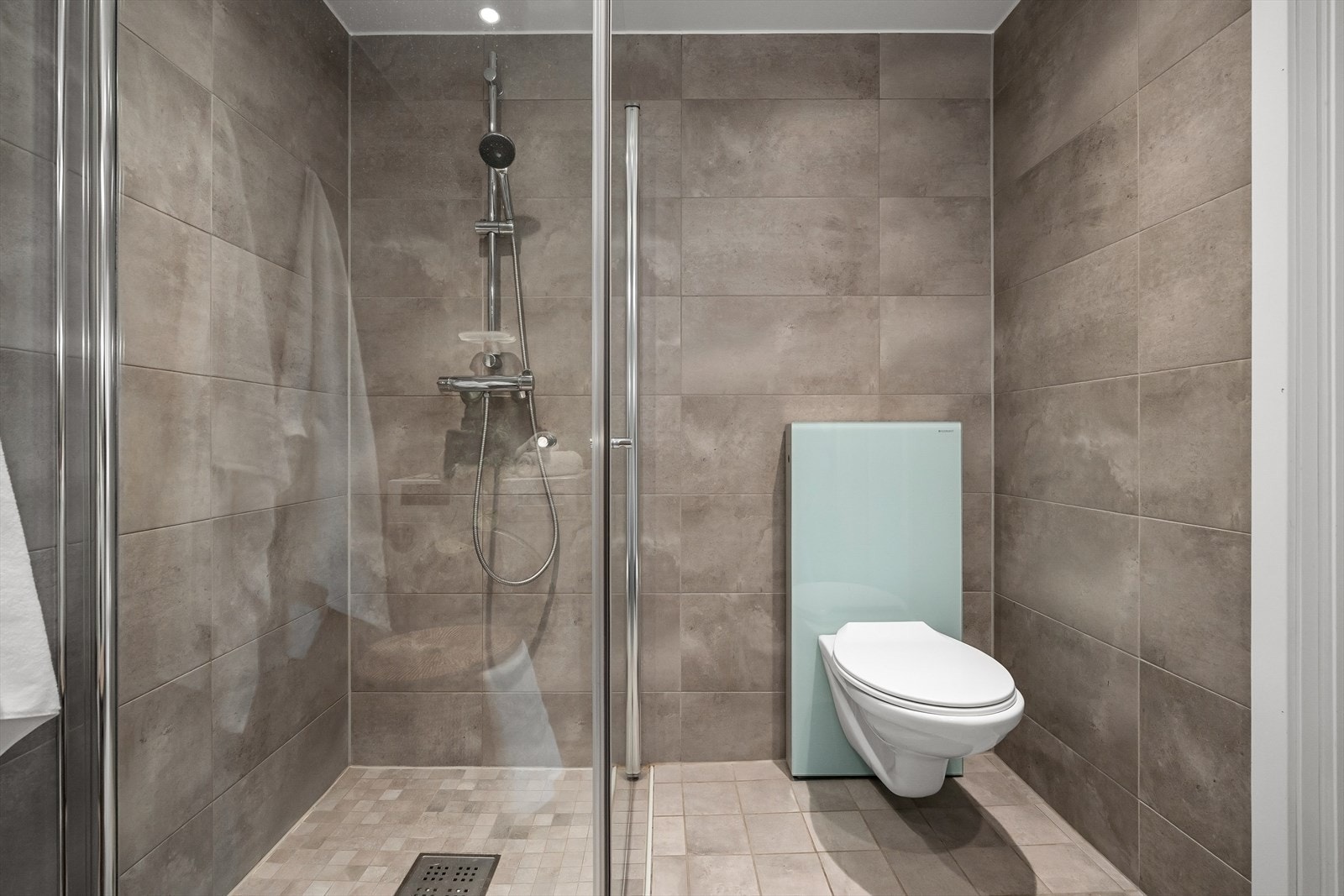 Badet er innredet med praktisk dusjhjørne, vegghengt toalett, speil med lys og servant med oppbevaring. Galleribilde