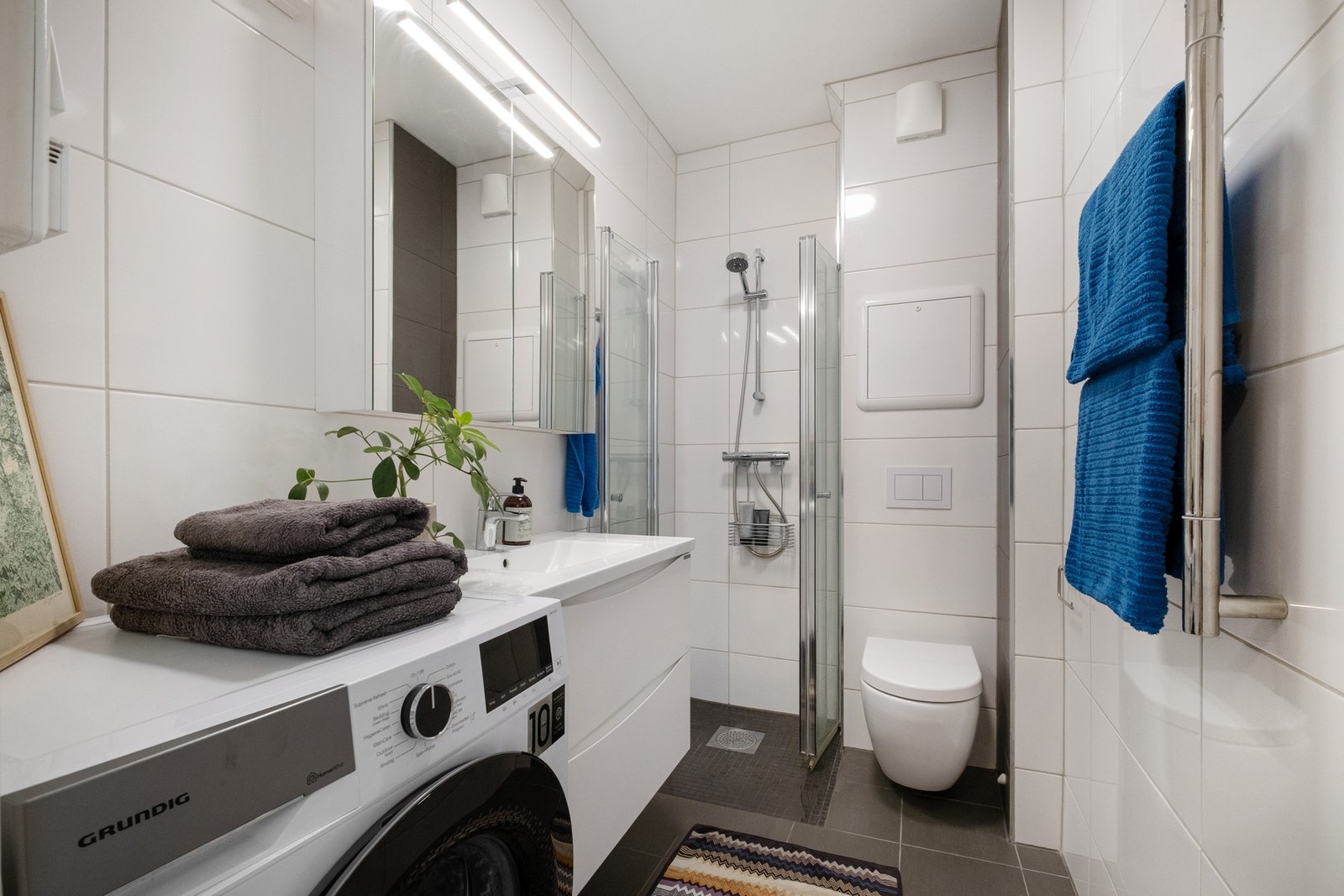 Leiligheten har et pent baderom fra 2019. Badet fremstår som romslig og funksjonelt, med flislagt gulv utstyrt med elektriske varmekabler som gir god komfort. Innredningen består av servant med underskap og tilhørende speilskap, vegghengt toalett og dusj. Galleribilde
