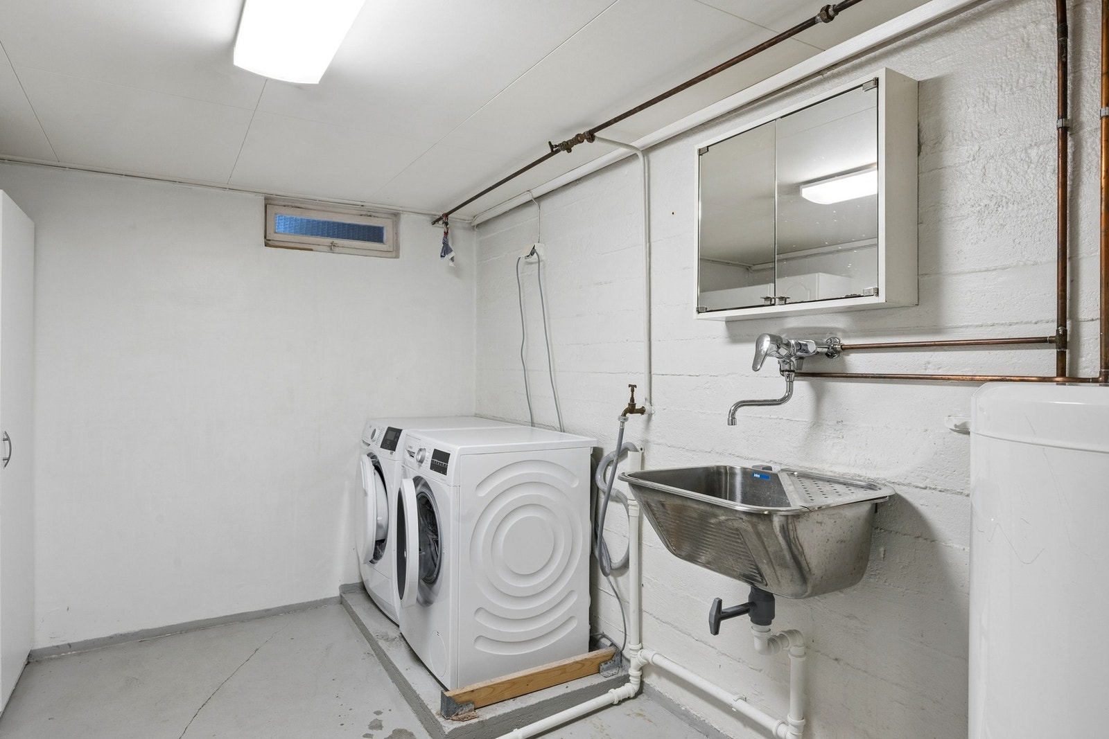 Praktisk vaskerom i kjelleren med opplegg for vaskemaskin, utslagsvask og malt betonggulv. Galleribilde