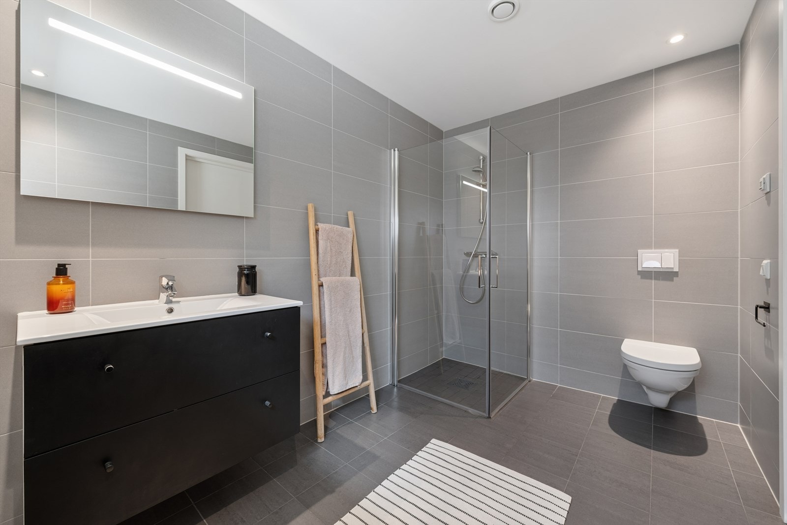 Badet i første etasje er helfliset og utstyrt med vegghengt toalett og dusjhjørne med glassvegger. Galleribilde