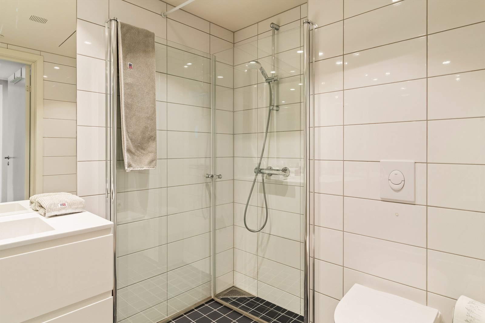 Det andre badet inneholder innredning med nedfelt servant, veggmontert toalett, dusjvegger og opplegg for vaskemaskin Galleribilde