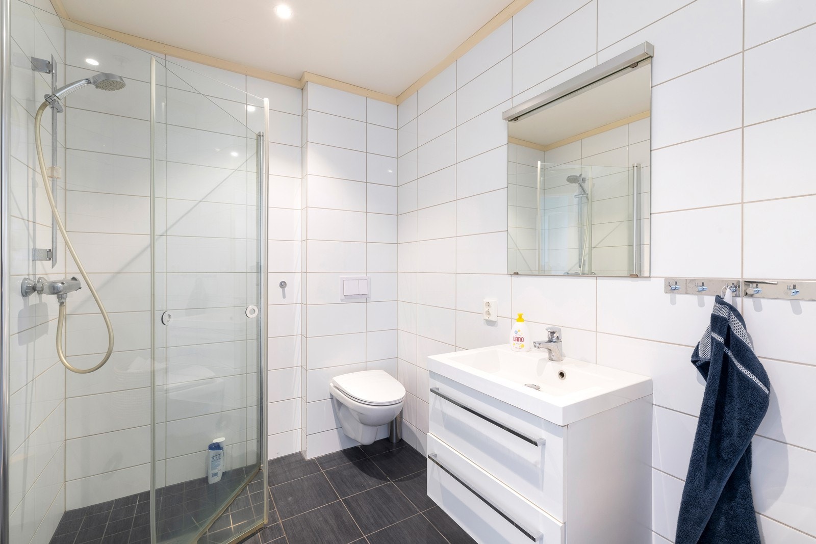 Flislagt bad med varme i gulv. Badet har dusjkabinett, servant med underskuffer og vegghengt toalett. Galleribilde