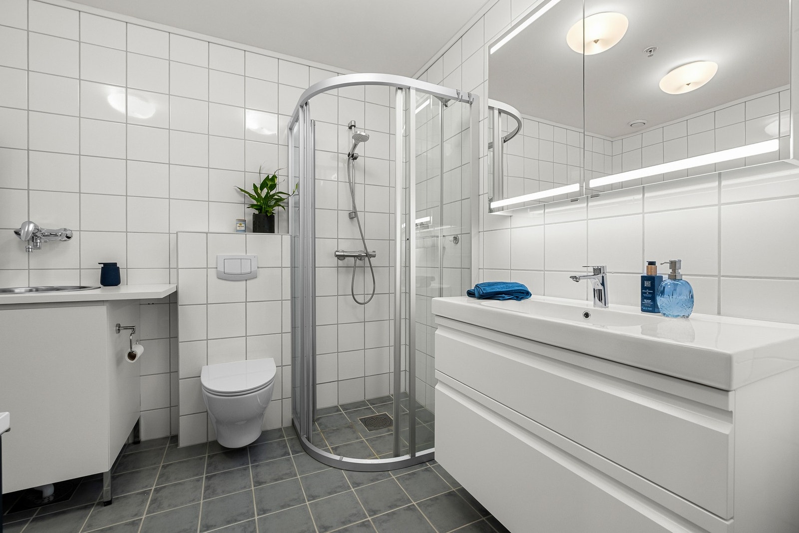 Badet er utstyrt med servant m/skuffer, speil, wc, opplegg for vaskemaskin og dusjhjørne. Galleribilde
