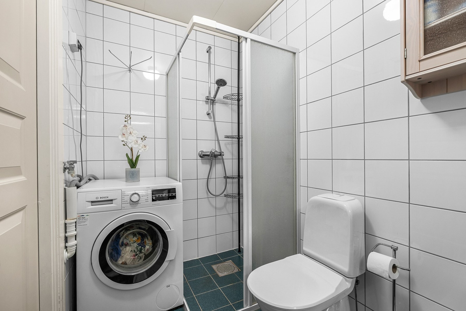 Badet er innredet med veggmontert servant og skapinnredninger, gulvmontert toalett, dusjnisje og opplegg/avløp for vaskemaskin Galleribilde