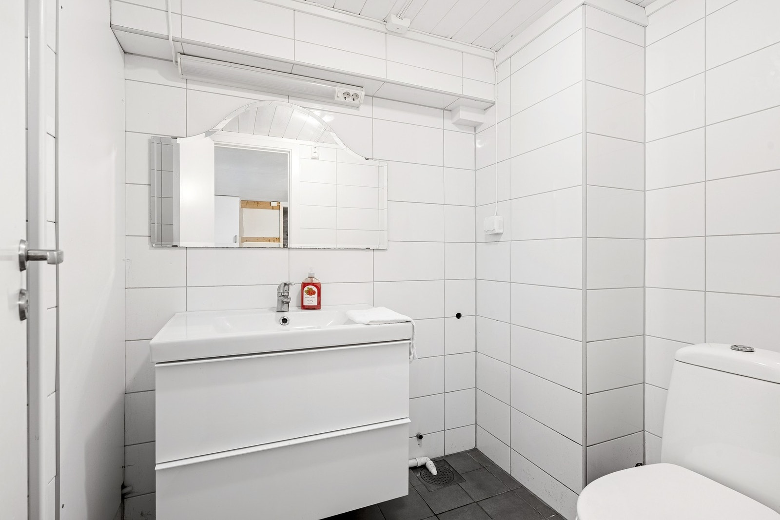 Lyst bad med fliser på vegger og gulv, samt enkel servant og toalett. Galleribilde