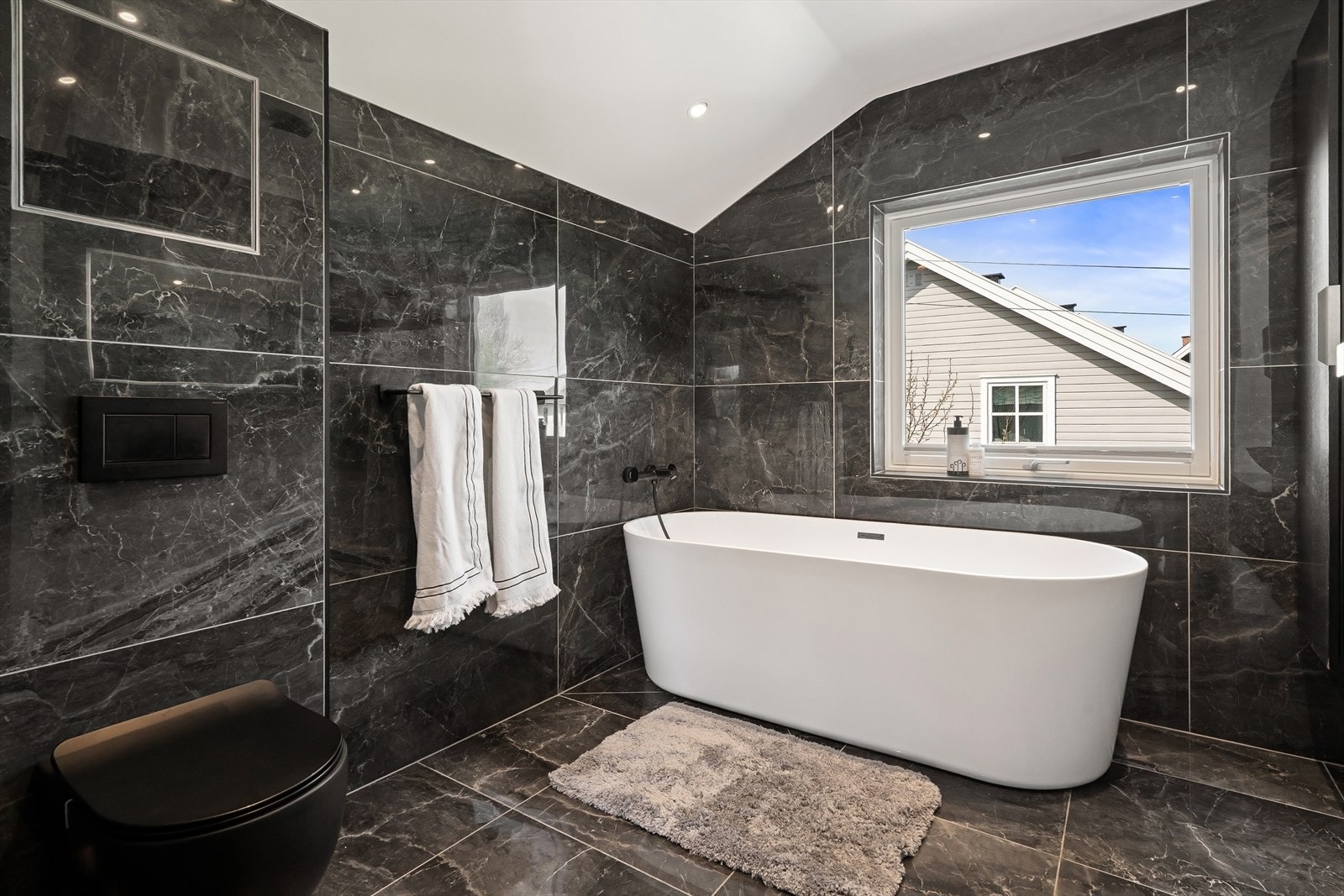 Delikat og romslig bad med store fliser, frittstående badekar og vegghengt toalett. Galleribilde