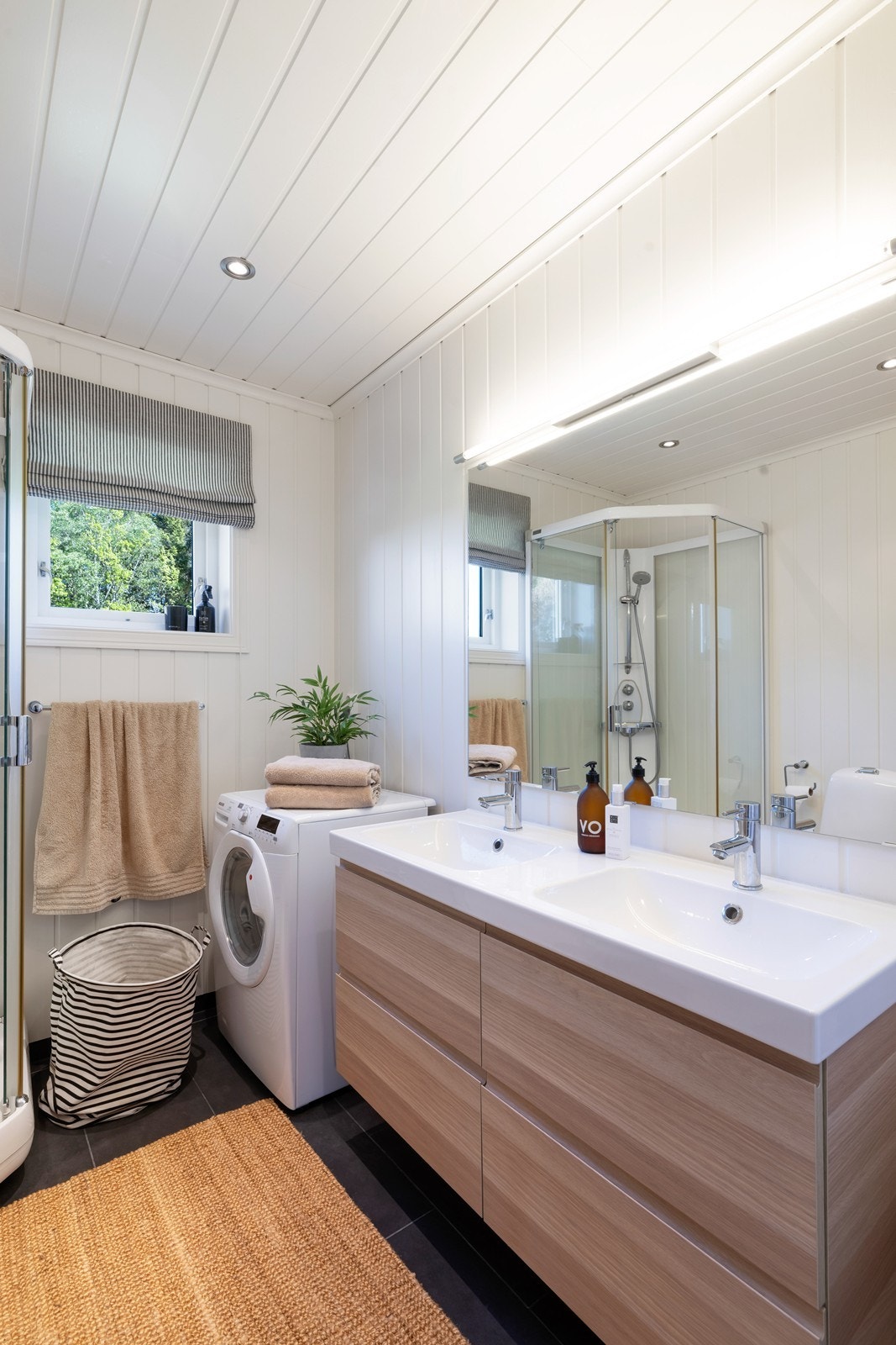 Flislagt bad med varme i gulv. Badet har dusjkabinett, dobbeltservant med underskuff, toalett og opplegg til vaskemaskin. Galleribilde