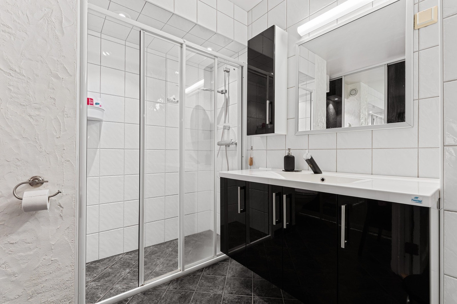 Badet er utstyrt med veggehengt toalett, dusj, heldekkende servant, samt baderomsinnredning. Galleribilde