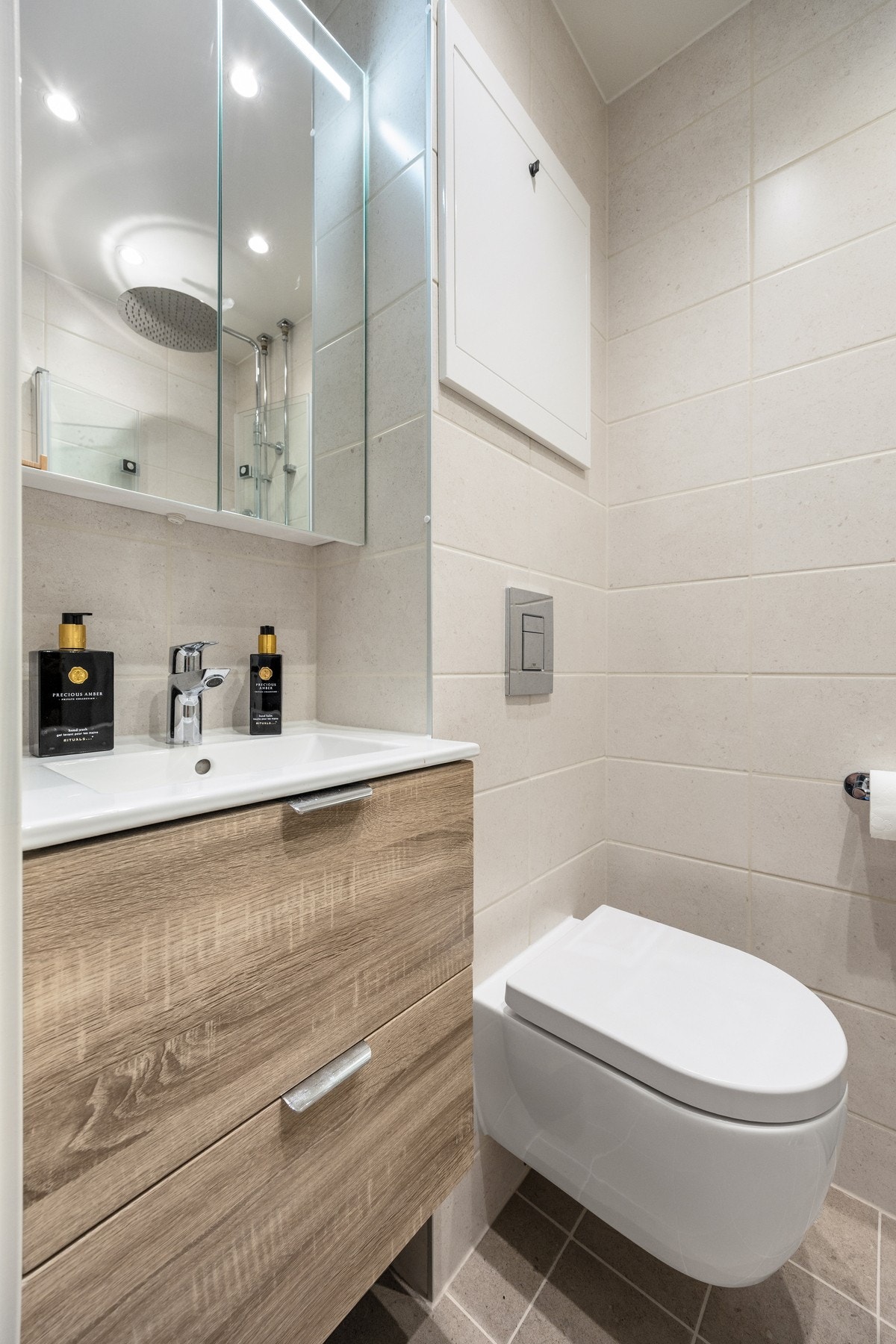 Badet har flislagte overflater og varmekabler i gulv. Innredningen består av stilrent servantmøblement, speilskap med integrert belysning og vegghengt toalett. Galleribilde