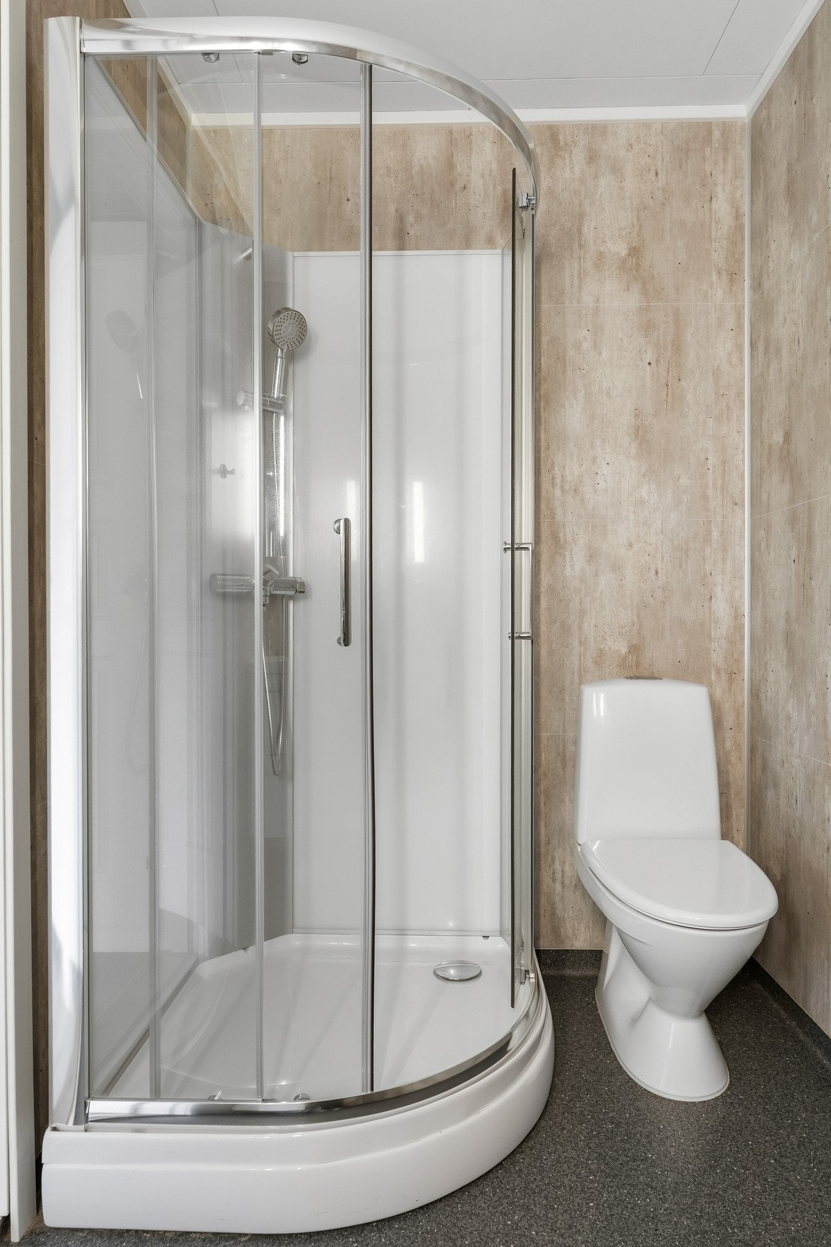 Videre har badet dusjkabinett og gulvstående toalett. På gulvet er det vinylbelegg og baderomsplater på vegg. Galleribilde