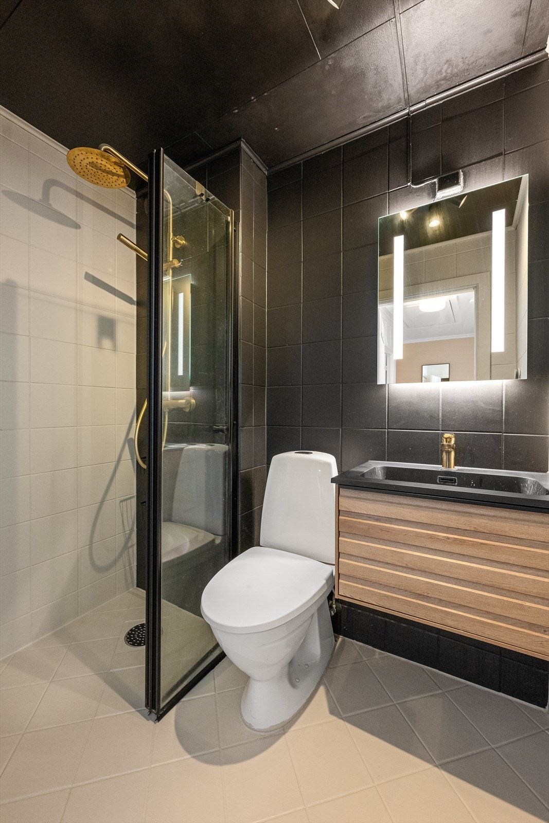 Badet er oppgradert med nyere baderomsinnredning bestående av en moderne skuffeløsning med gullarmatur, dusjvegg og et tilhørende speil med integrert belysning. Galleribilde