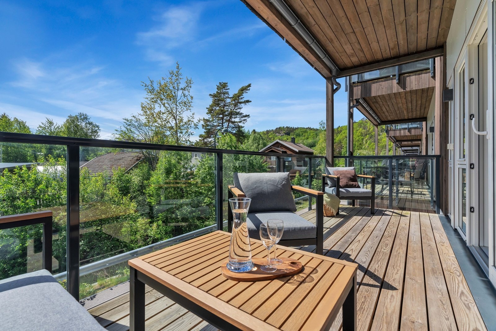 Gulvet er belagt med terrassebord, og rekkverket i glass og metall gir en åpen og luftig følelse, samtidig som det bevarer utsikten mot de omkringliggende grøntområdene. Galleribilde