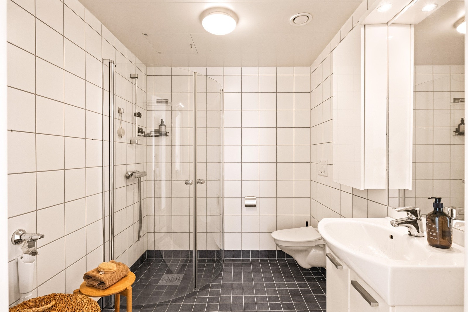 Romslig og fint baderom med flislagt gulv med varme og flislagte vegger. Baderommet nedsenket himling med malte plater og vegghengt servantskap med glatte fronter. Galleribilde