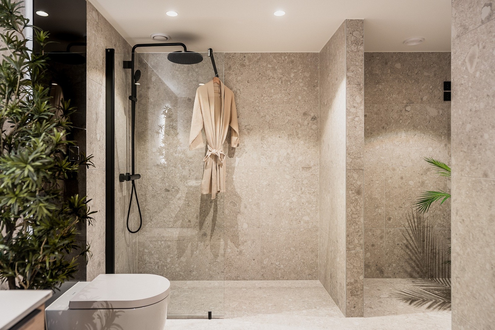 Dusjhjørnet er nedsenket og utstyrt med sort armatur og glassvegg . Badet har opplegg for vaskemaskin og tørketrommel i en praktisk nisjeløsning som er delvis skjermet fra resten av badet. Galleribilde