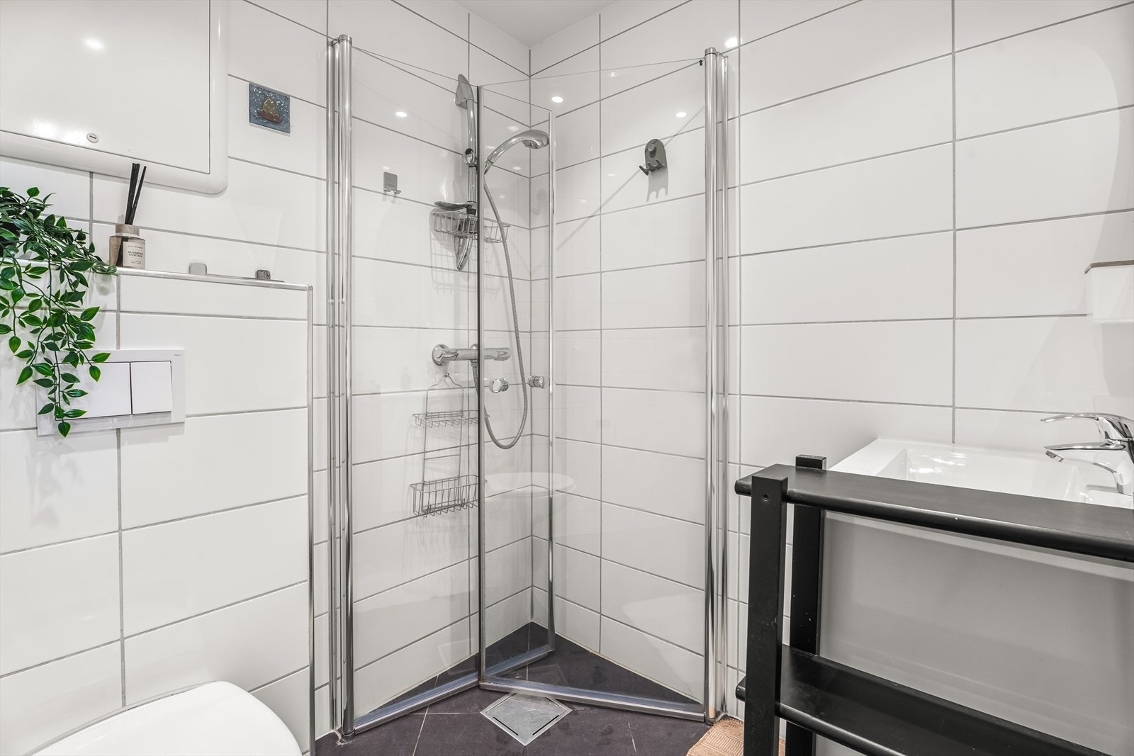 Badet er innredet med vegghengt toalett, servant nedfelt i baderomsinnredning samt dusjhjørne med svingbare glassdører. Galleribilde