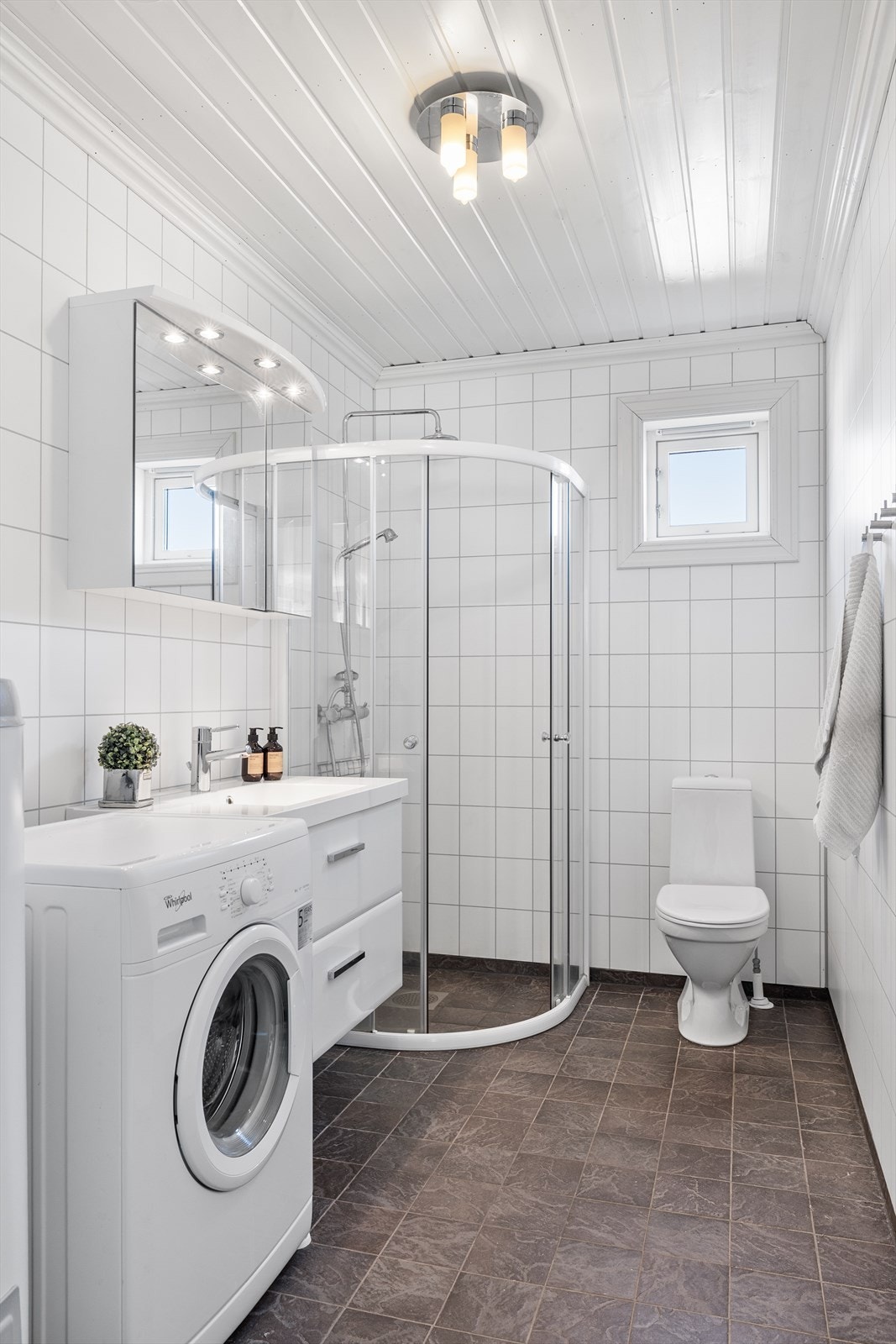 Badet har flisimiterte våtromsplater på vegg og malt panel i tak, fliser på gulv, vaskeservant i innredning, toalett og dusj. Galleribilde