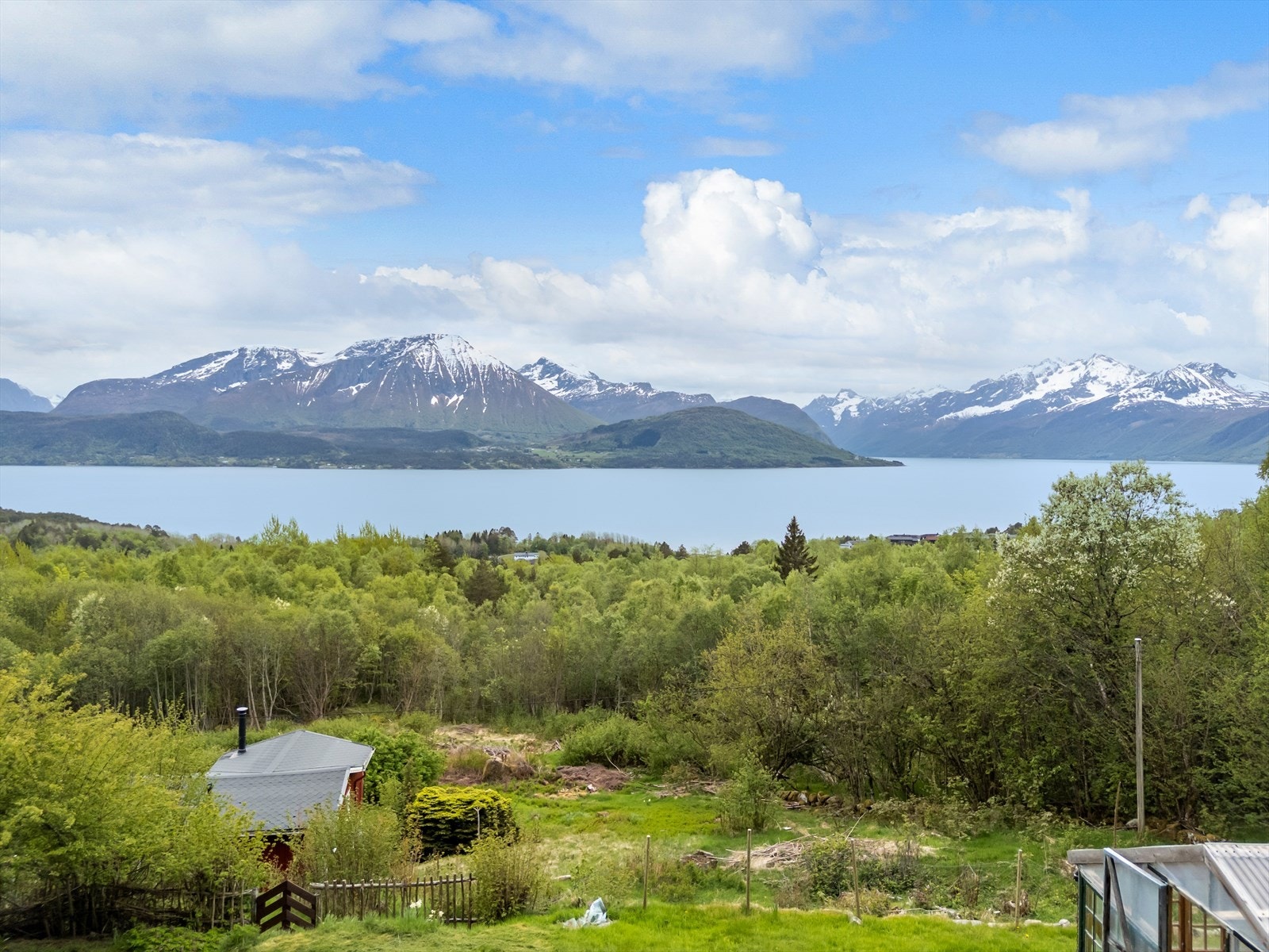 Eiendommen ligger i en fjellside med utsikt over fjord og fjell, omgitt av natur. Galleribilde