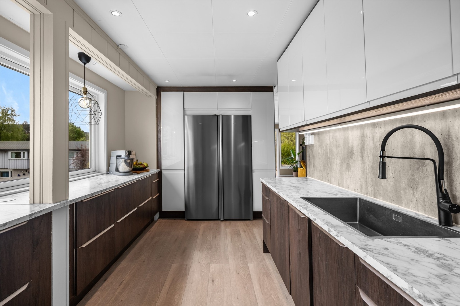 Stilfullt kjøkken med stort side-by-side kjøleskap, betonglignende fliser som bakvegg og elegant sort blandebatteri - en moderne og praktisk løsning for den matglade. Galleribilde