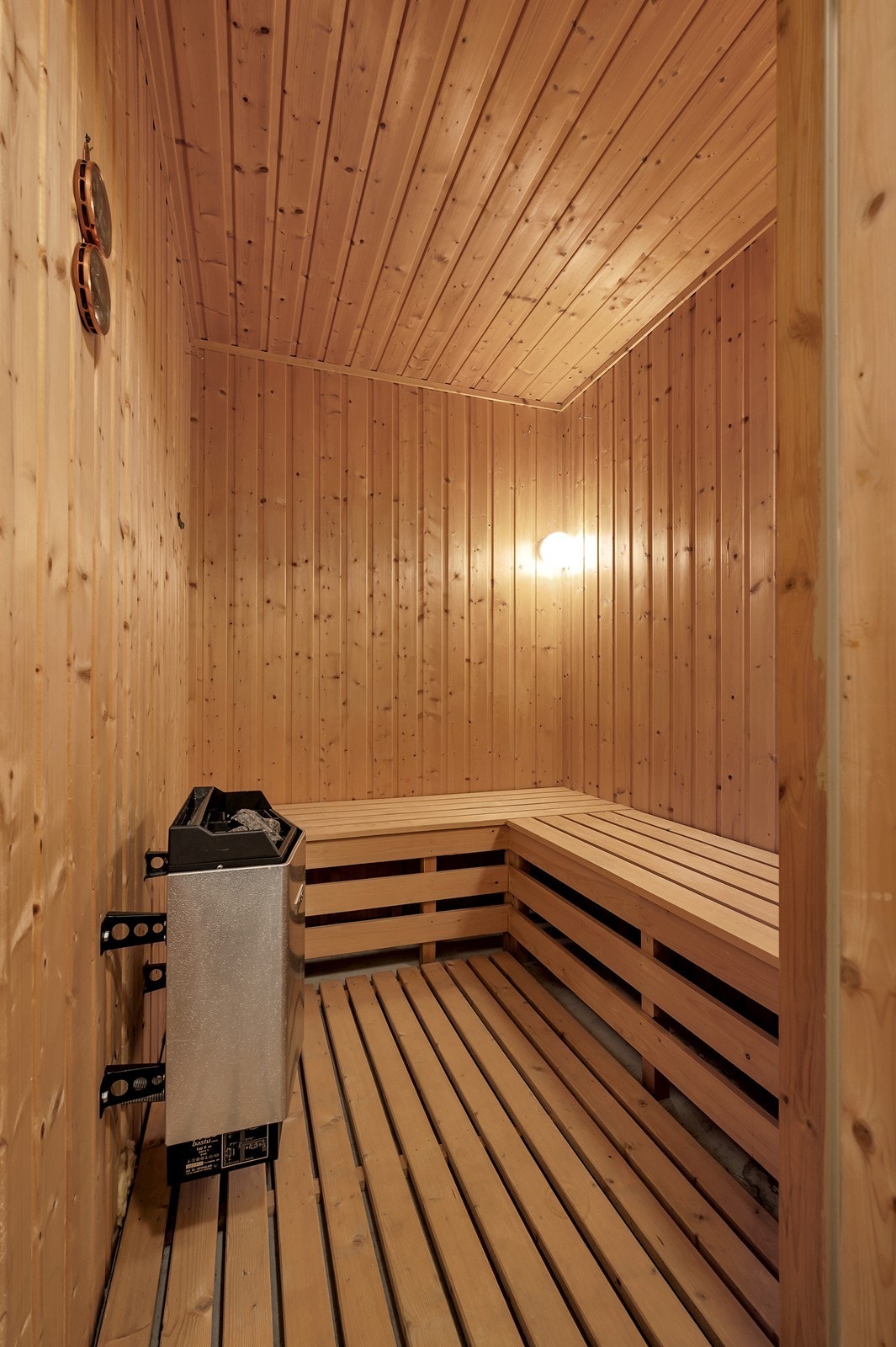 Badstuen har gulv av mur med løse trepaller og vegger med panel, samt en elektrisk badstuovn for oppvarming. Galleribilde