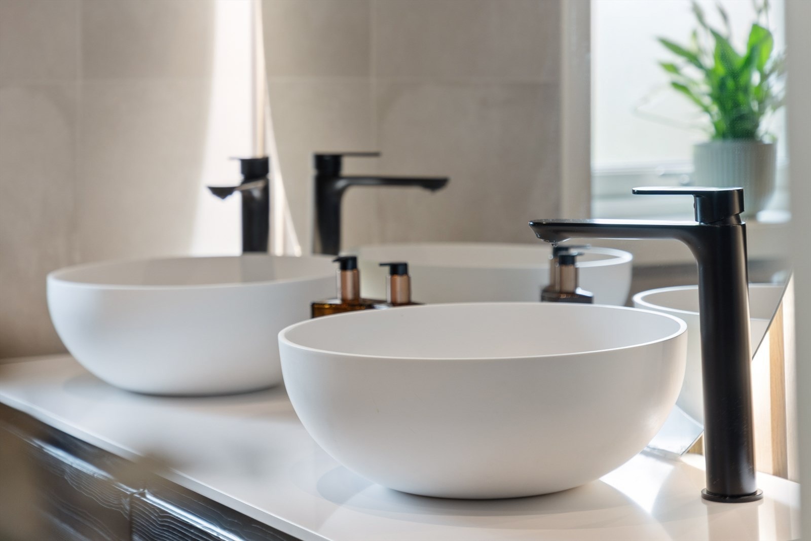 Detaljer fra badet med moderne, frittstående servanter og sorte armaturer. Det er montert strømuttak i skuffer for hårføner og barbermaskin. Galleribilde