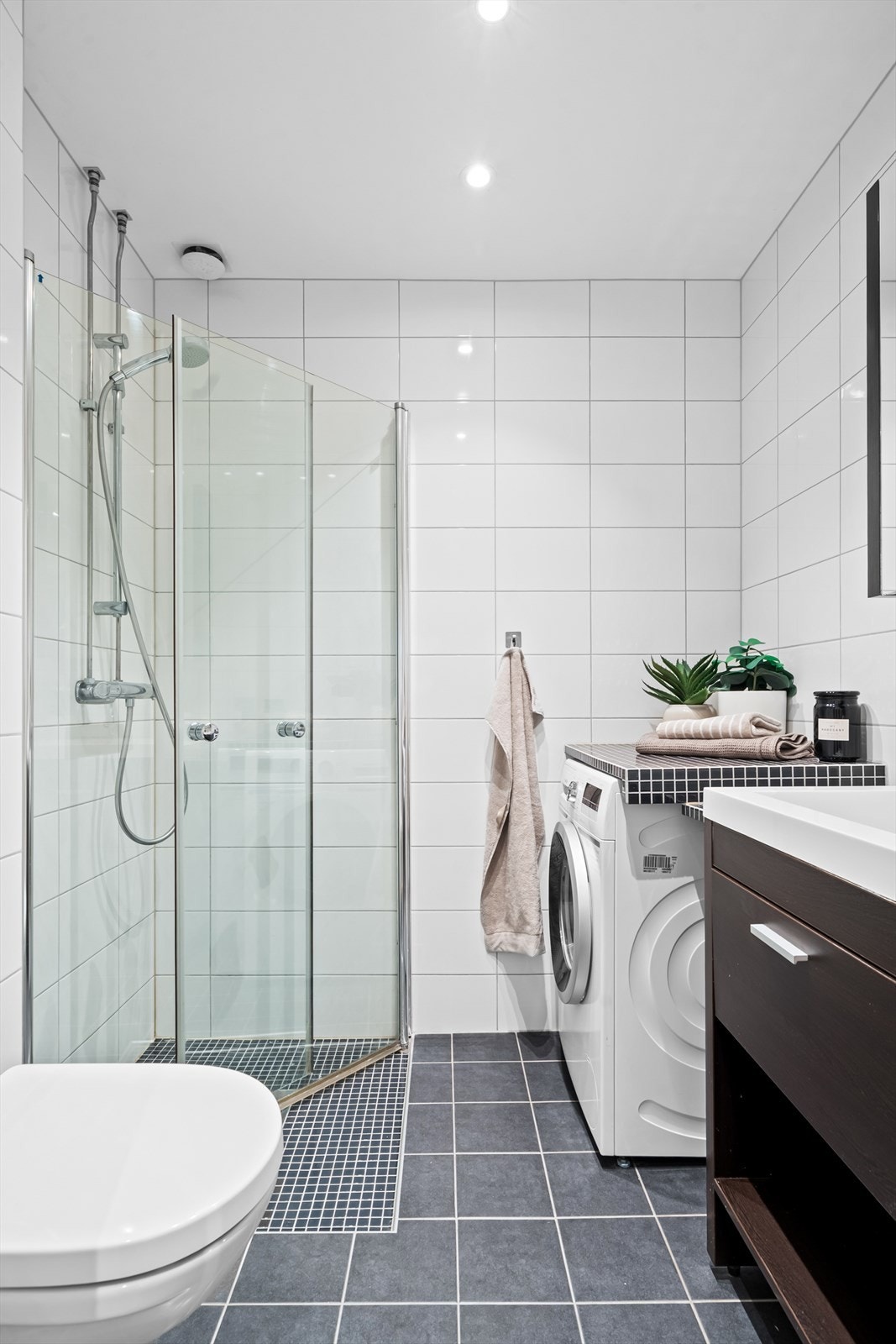 Badet er innredet med benkeskap med glatte fronter og veggskap med speilfronter, dusjhjørne og toalett. Det er opplegg for vaskemaskin i hjørnet. Galleribilde