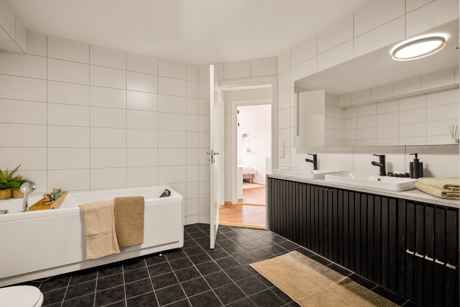 Lyst og tidløst baderom med stor dobbel servantinnredning, speil, badekar, dusjhjørne og toalett. Galleribilde