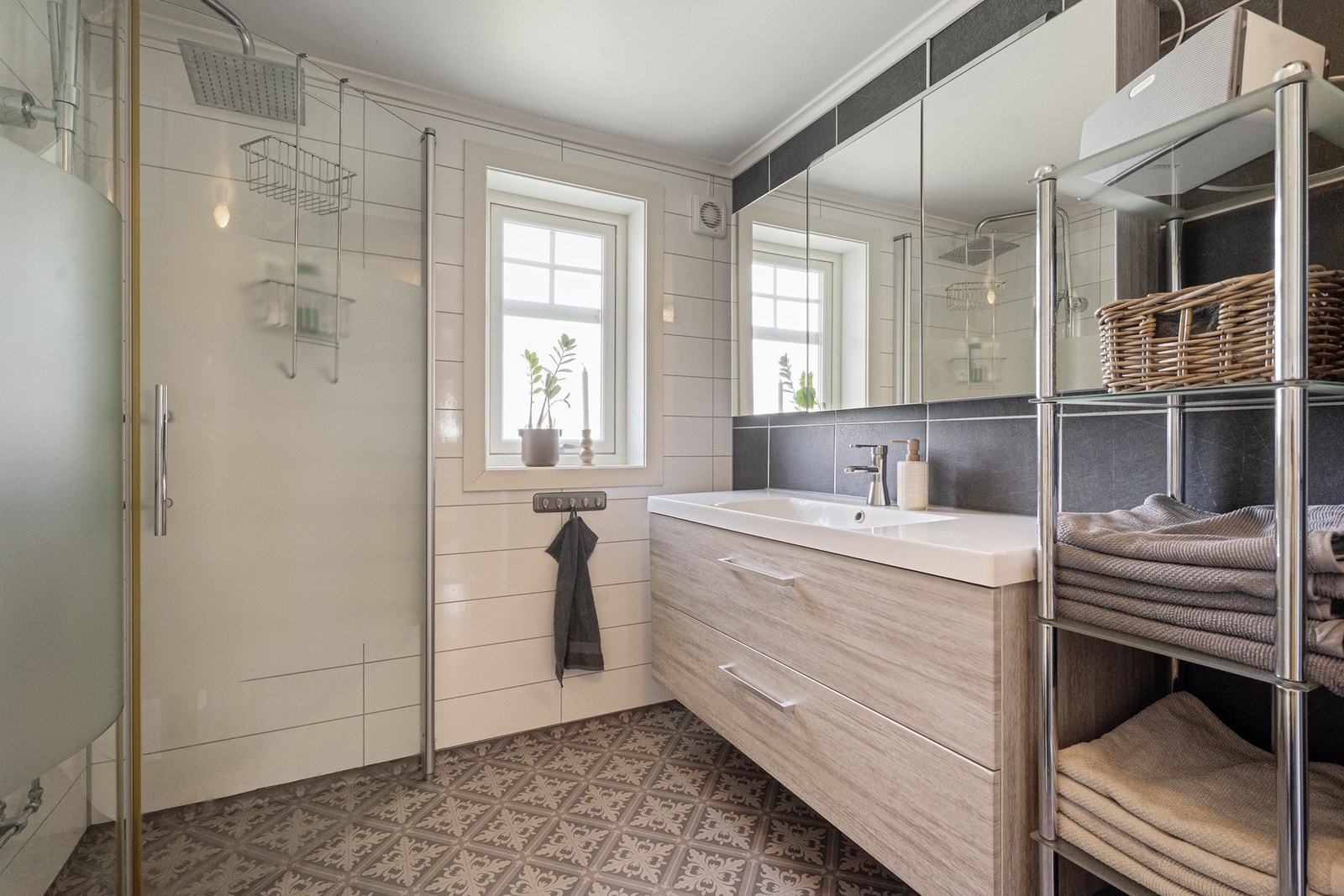 Badet fremstår praktisk og funksjonelt med gulvvarme, dusjhjørne med glassdører og moderne innredning med heldekkende servant. Galleribilde