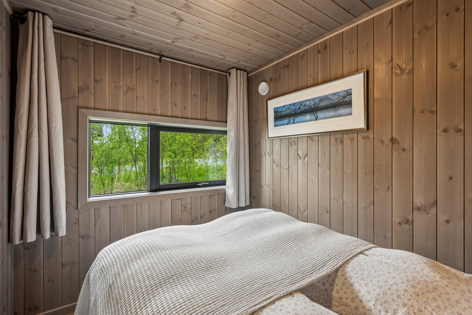 Lunt soverom med panelkledde vegger og vindu som gir lysinnslipp. Galleribilde