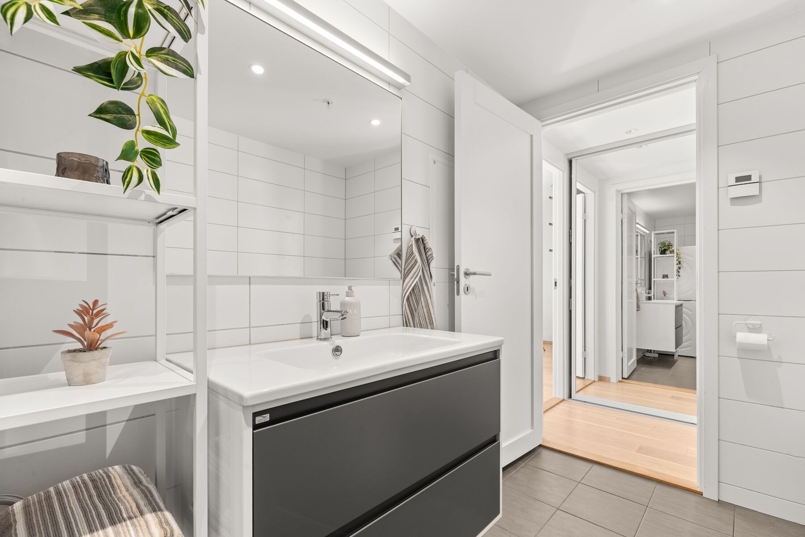 Badet har dusjvegger av glass., vegghengt toalett og innredning med servant, Opplegg for vaskemaskin Galleribilde