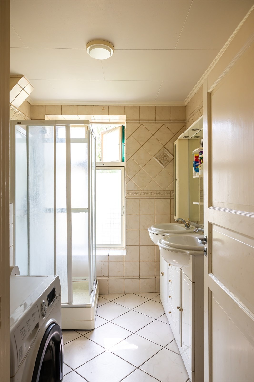 Flislagt bad med varmekabler i gulvet. Badet er utstyrt med dobbel servant, vegghengt toalett, dusjkabinett og opplegg for vaskemaskin. Galleribilde
