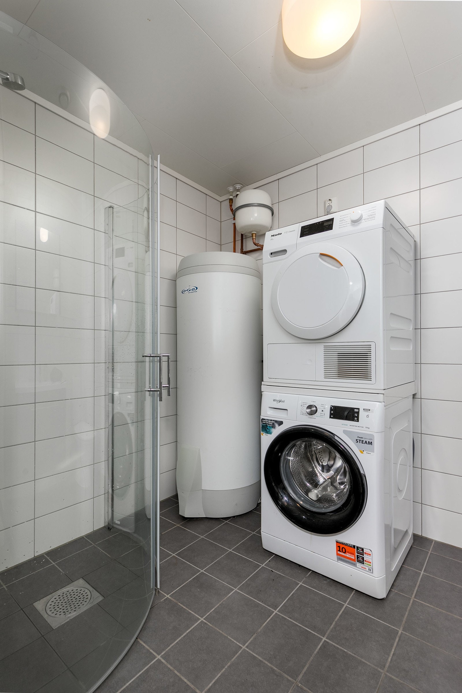 Badet har dusjhjørne med innfellbare dører og gulvstående toalett. Opplegg for vaskemaskin og tørketrommel. Galleribilde