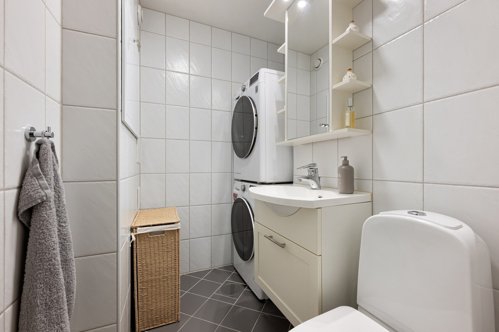 Vaskerom/toalettrom i underetasjen med flislagte overflater, servantskap, toalett og opplegg for vaskemaskin og tørketrommel. Galleribilde