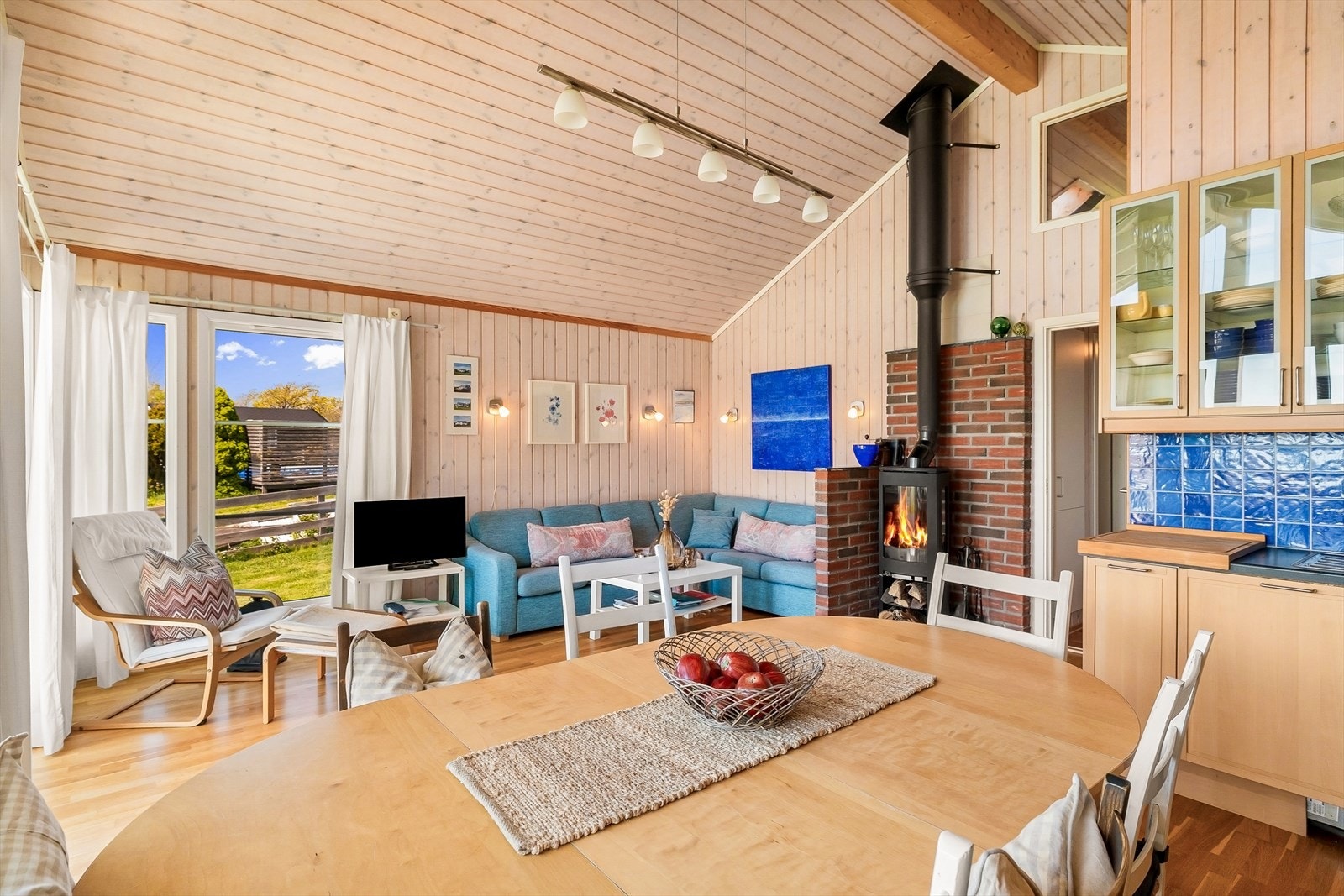 Stuen varmes opp av en vedovn montert mot en murt brannvegg, med isolert stålpipe. Galleribilde