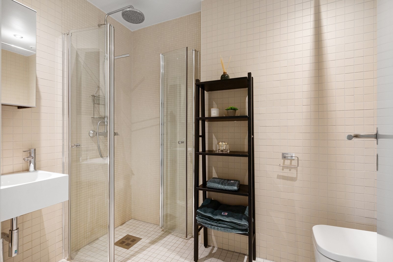 Badet er innredet med gulvstående toalett, dusjhjørne med vegger/dører i herdet glass, servant med skap, speil og belysning, samt opplegg for vaskemaskin. Galleribilde