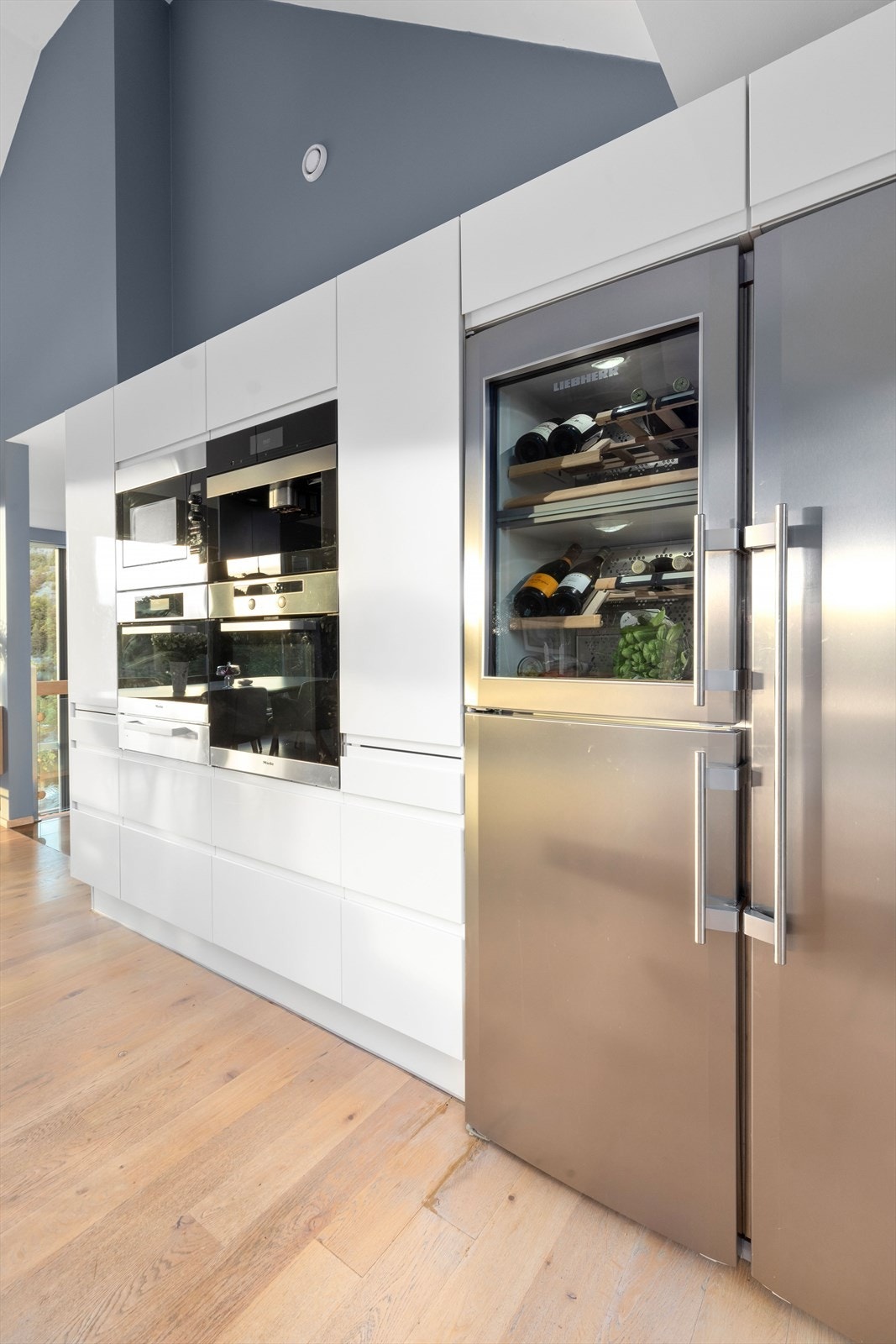 Hvitevarer som ovn, platetopp og gassbrenner med vifte, dampovn, tallerkenvarmer, kaffemaskin og dobbelt Liebherr kjøleskap med vinskap medfølger salget. Galleribilde