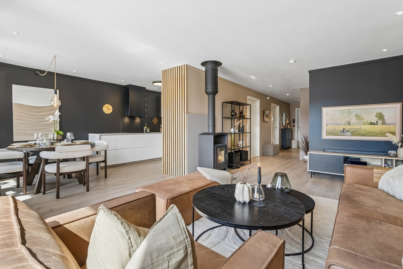 Den åpne løsningen gir en sosial sone med plass til både sofagruppe og spisebord. En moderne vedovn gir ekstra varme. Galleribilde