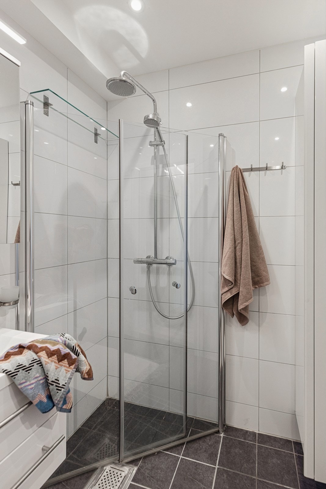 Dusjhjørne med innfellbare dusjvegger, rainshower og håndholdt dusj. Glasshylle på vegg. Veggskap. Galleribilde