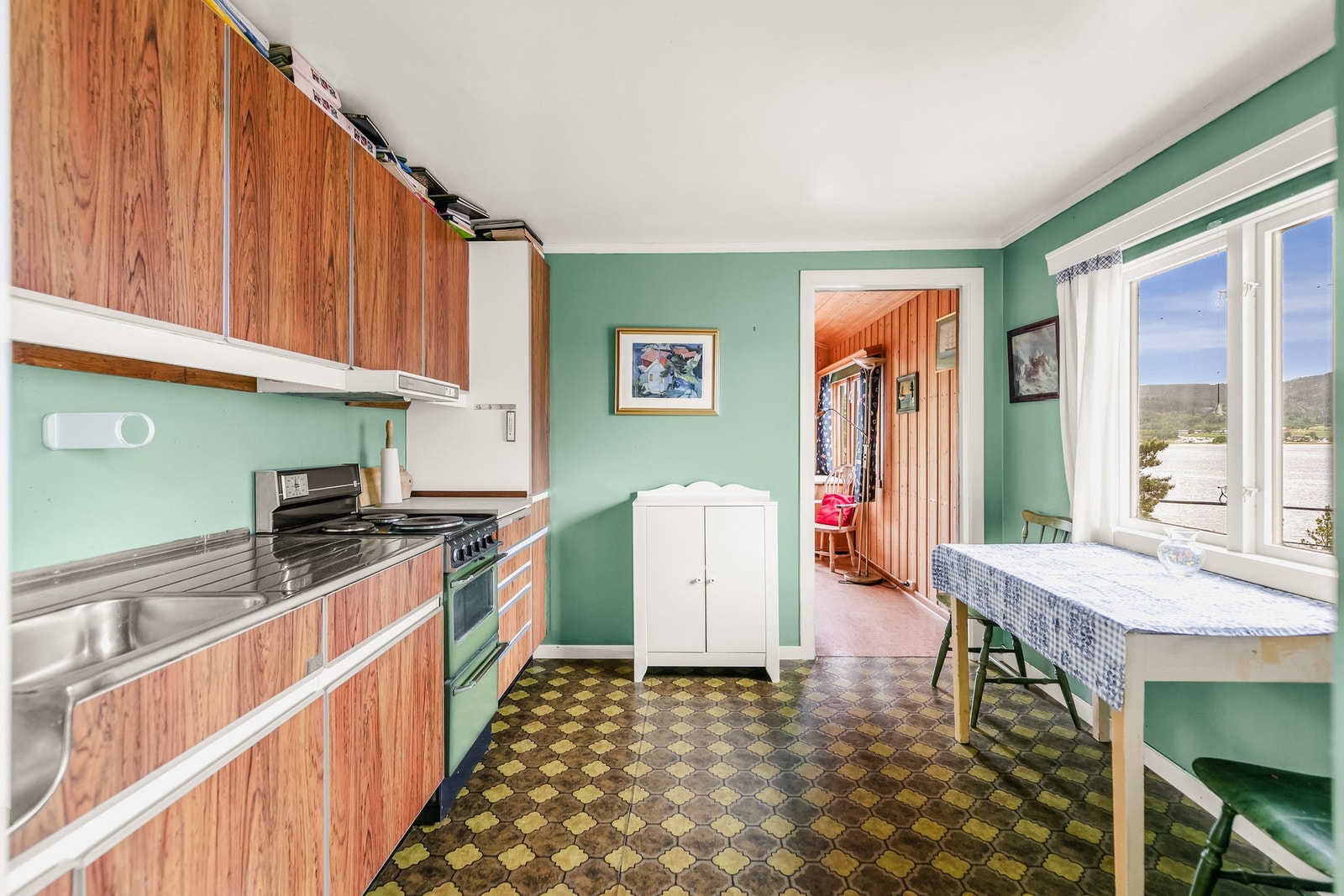 Kjøkken med innredning med glatte fronter og benkeplate av rustfritt stil med nedfelt oppvaskkum, samt benkeplate med laminert overflate og kjøkkenvask. Galleribilde