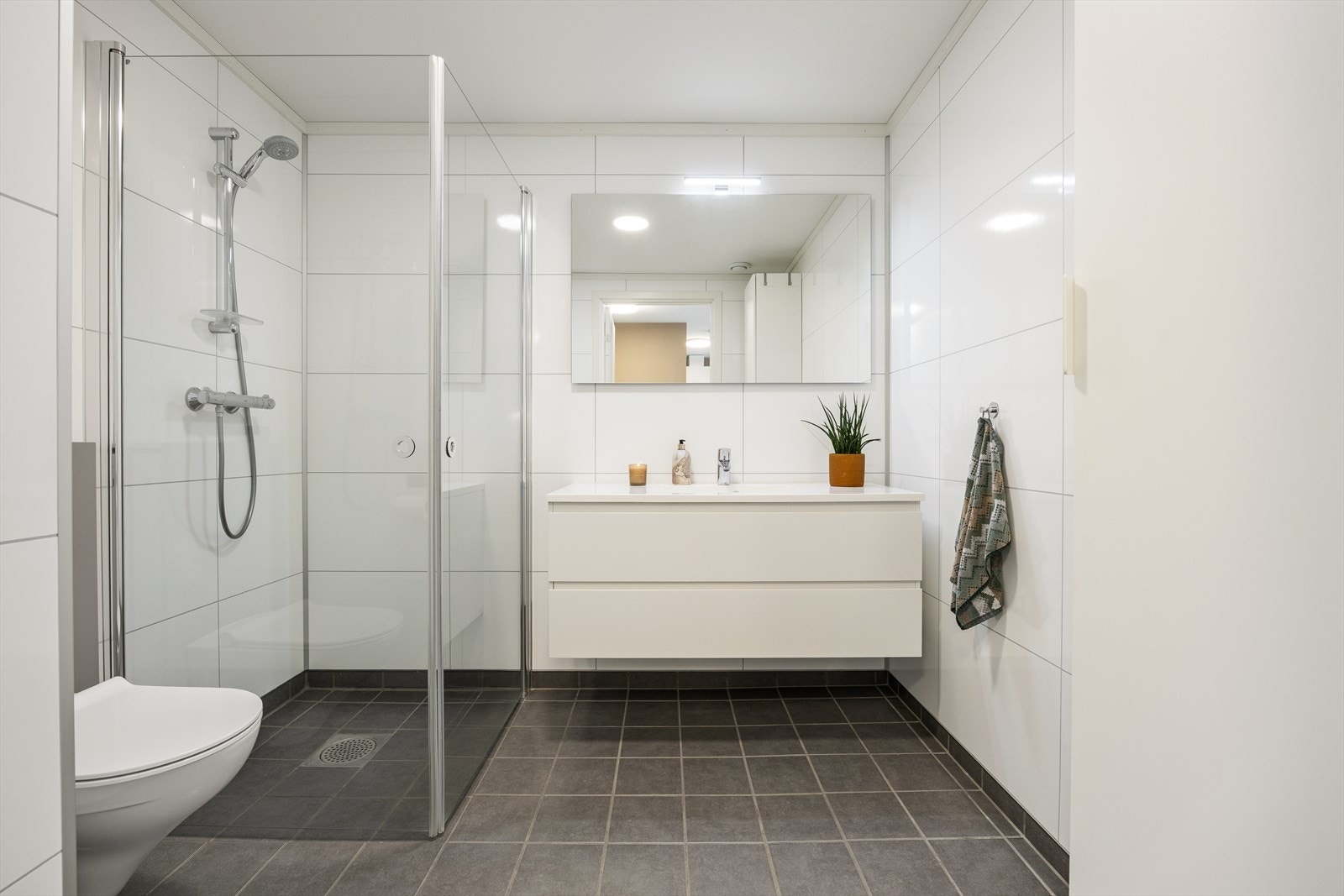Badet er tidløst innredet med grå fliser på gulvet og hvite baderomsplater på vegg. I gulvet har man også vannbåren varme for ekstra komfort. Galleribilde