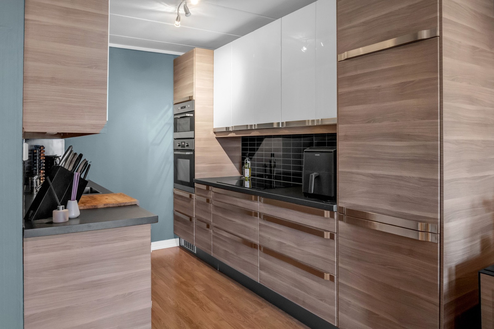 Kjøkkenet fremstår moderne og funksjonelt med en innredning som kombinerer mørke trefolierte fronter med lyse overskap. Galleribilde