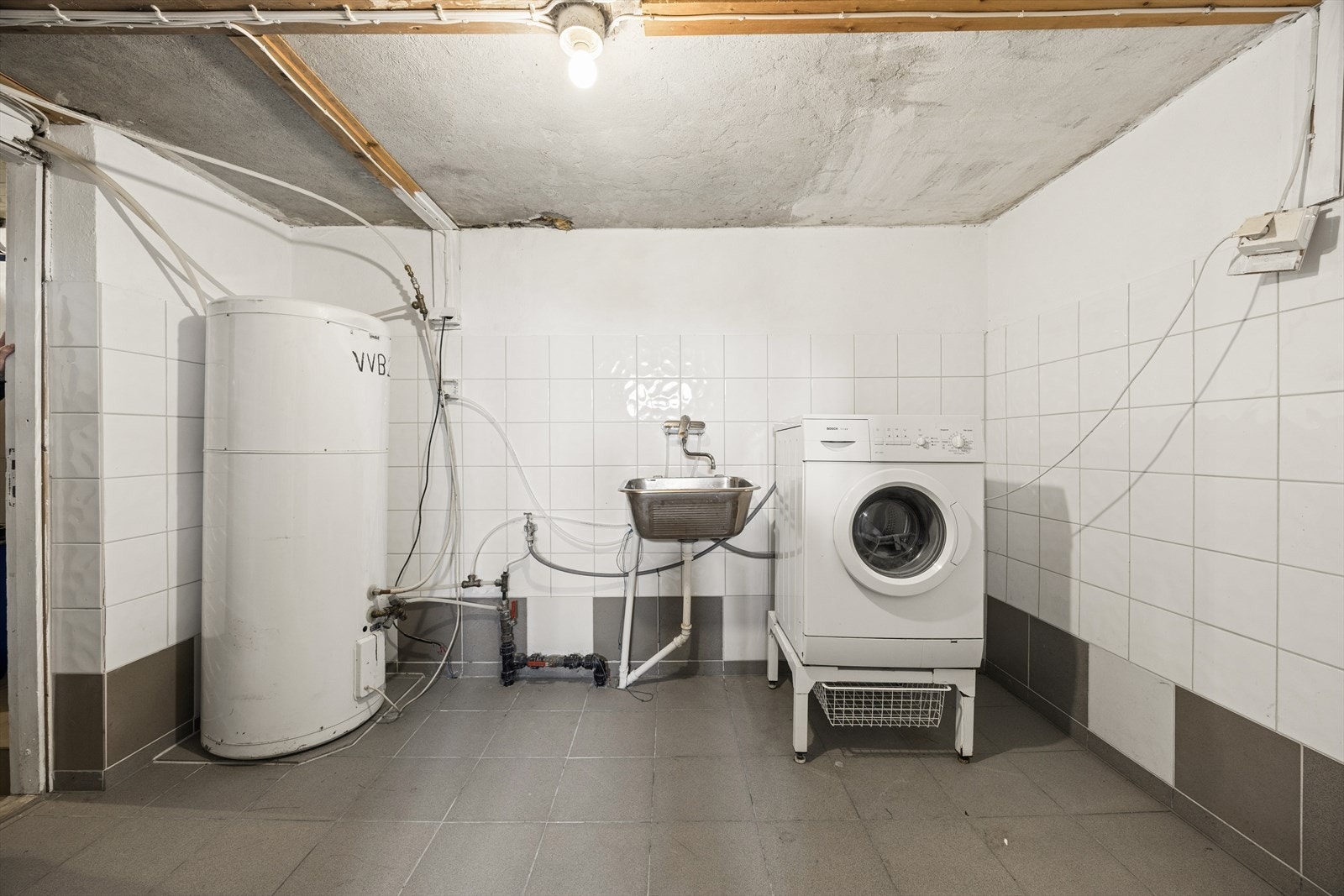 Vaskerom i kjeller med flislagt gulv med varmekabler, opplegg for vaskemaskin og skyllekar i stål. Galleribilde