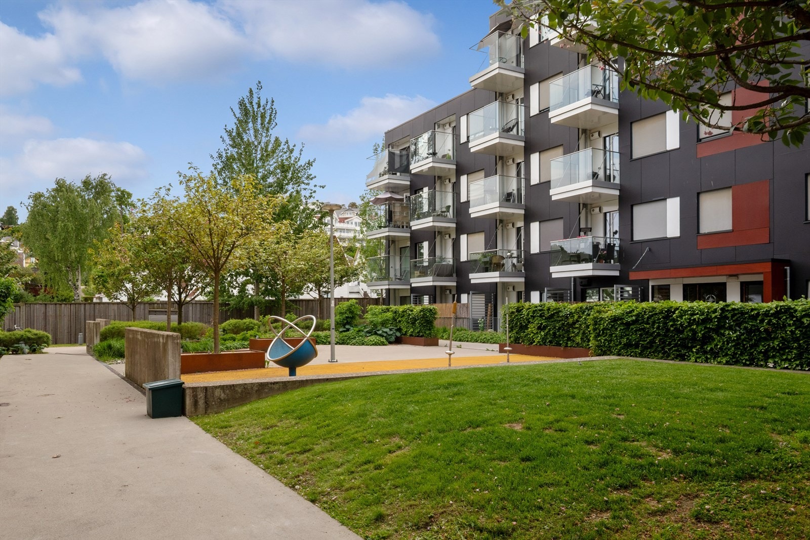 Pent opparbeidet fellesareal med grøntområder, blomsterbed og lekeplasser. Galleribilde