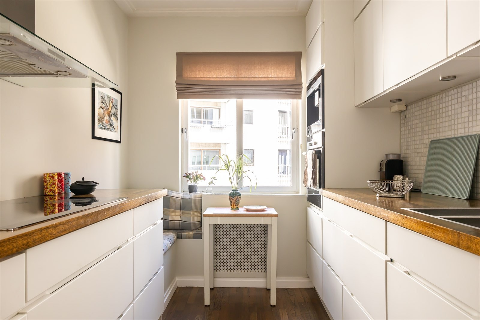 Pent kjøkken innredet med slette fronter og benkeplate av tre. Utstyrt med integrert stekovn, platetopp, kaffemaskin, oppvaskmaskin og kjøl/fryseskap. Galleribilde