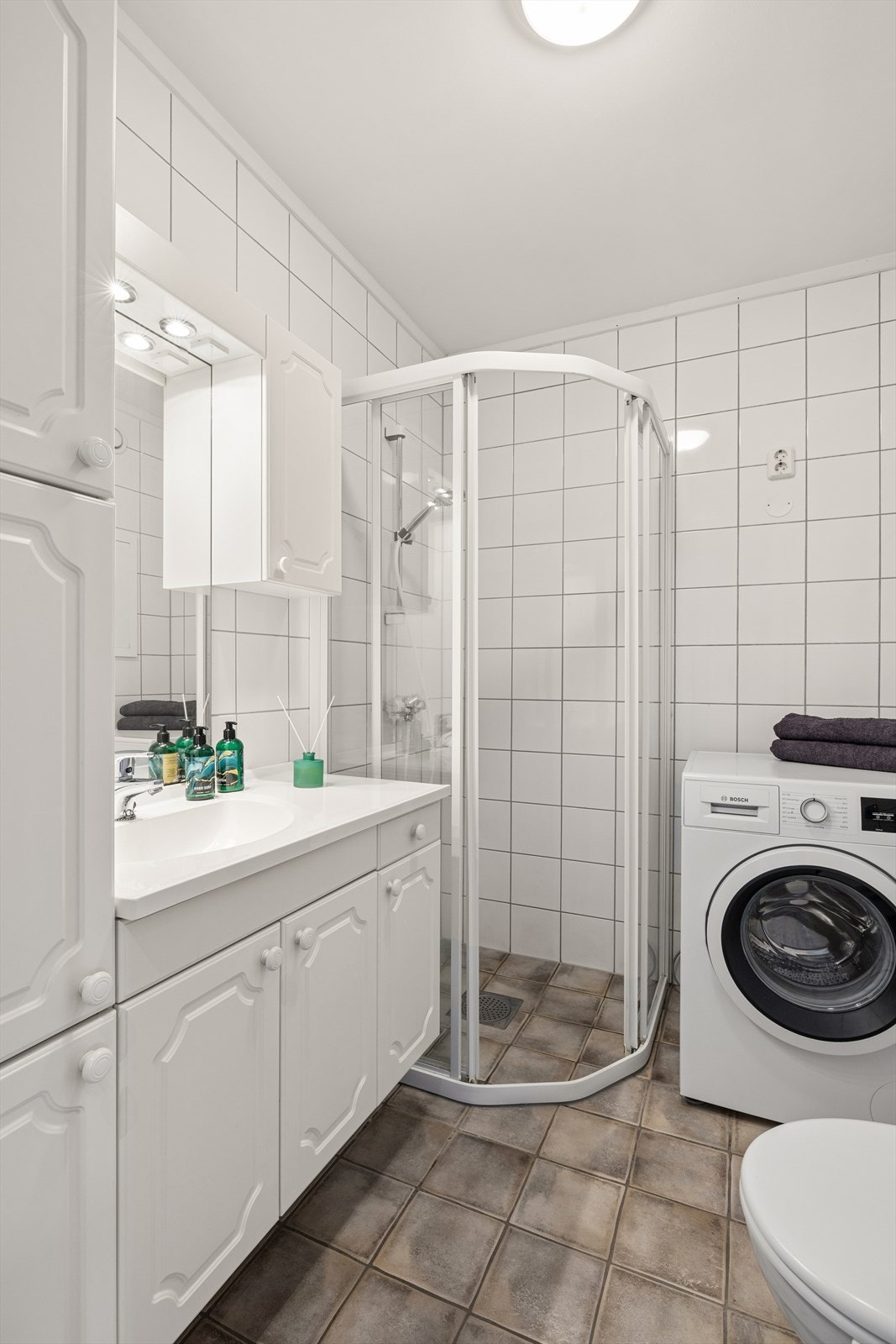 På badet er det montert servantskap med steinplate og servant i ett, dusjhjørne med glassdører, vegghengt toalett og opplegg for vaskemaskin. Galleribilde